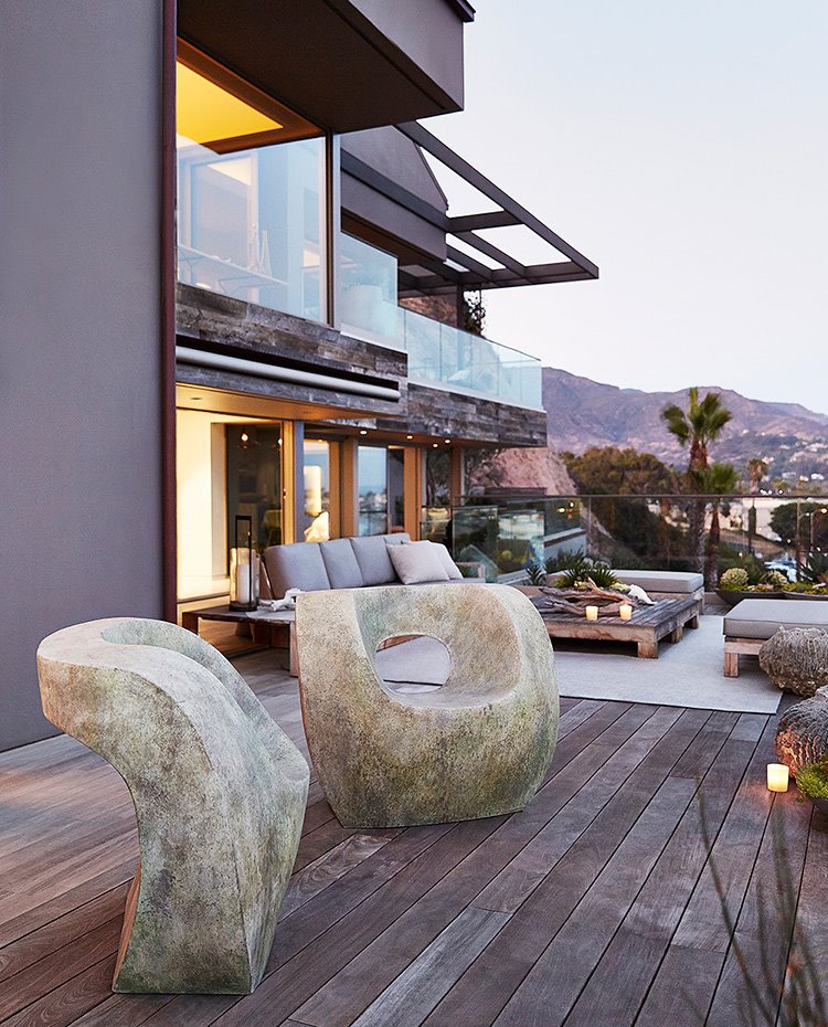 Terraza exterior con tarima de madera, asientos de piedra, alfombra de color crudo, mesa y sofás con estructura de madera