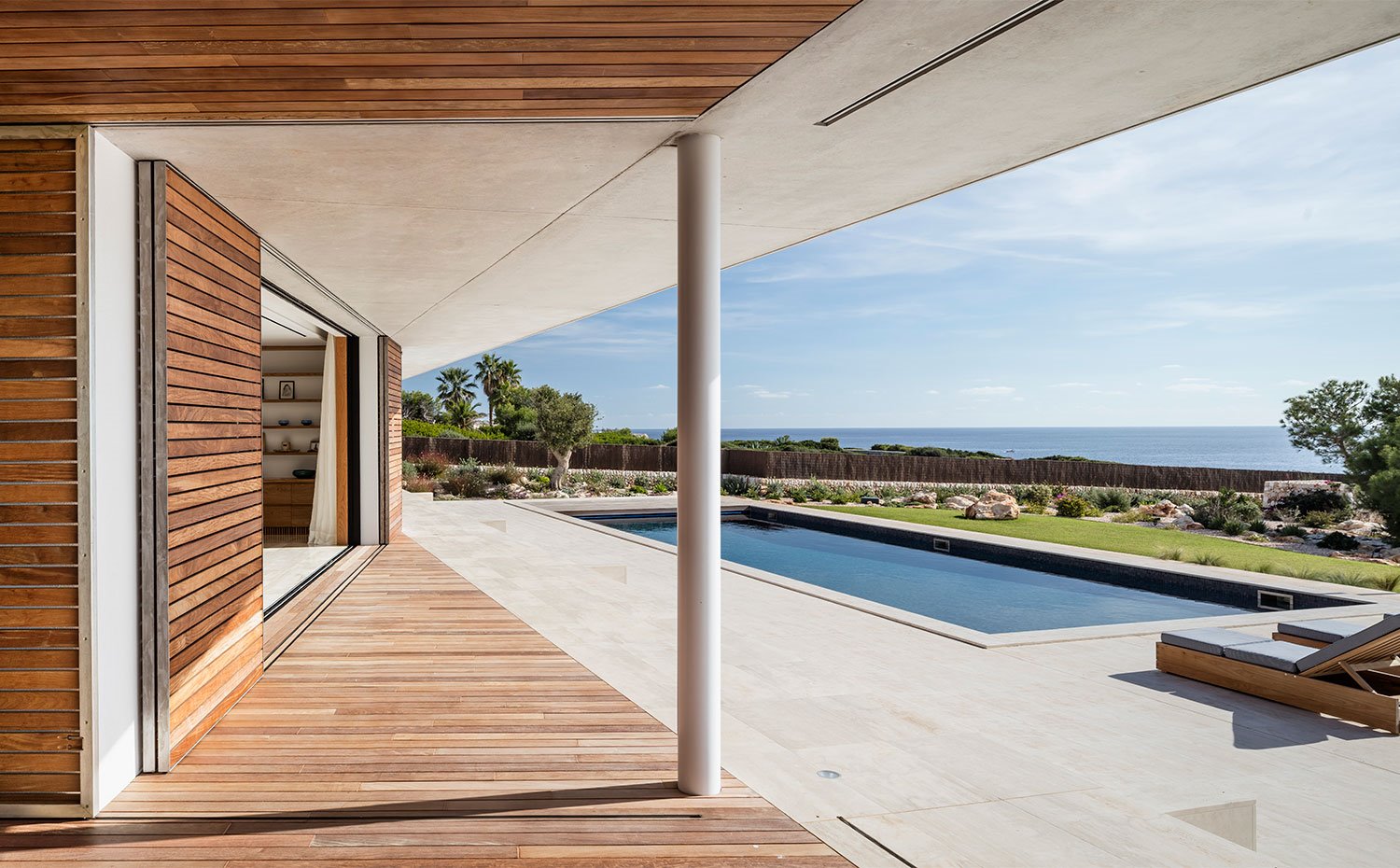 Apertura del interior hacia la terraza exterior con piscina rectangular y tumbonas de madera