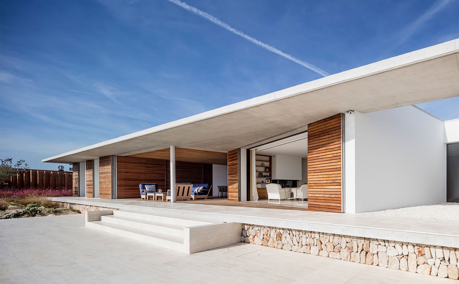 Salón exterior e interor abiertos a la terraza con escaleras que salvan el desnivel hacia piscina