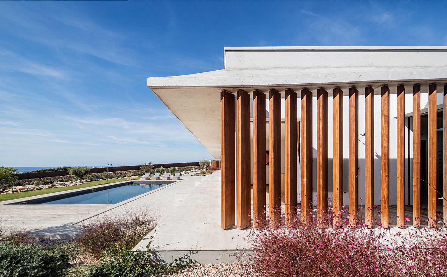 Vista exterior de la vivienda con piscina, estructura de vivienda en hormigón con listones de madera, 