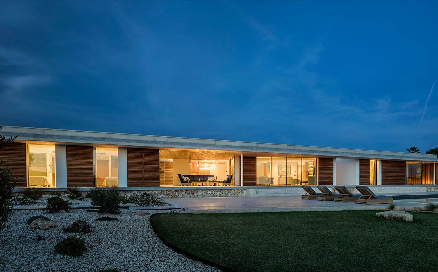 Vista exterior nocturna vivienda con tumbonas y salón exterior