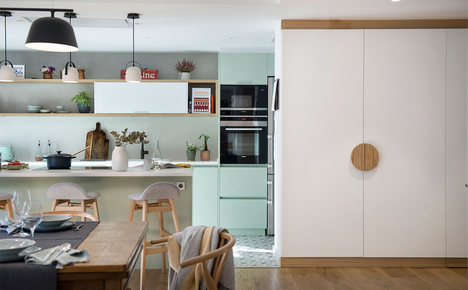 Cocina abierta en color verde menta, suelo baldosa hidraulica, frente de armarios en blanco con tirador en forma de círculo de madera natural