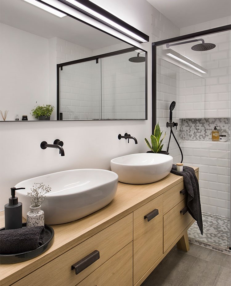 Cuarto de baño con doble lavamanos sobre mueble en madera, revestimiento en blanco y luminarias acabadas en negro