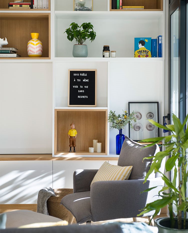 Detalle librería en madera con hornacinas en acabado natural, butaca con cojín a rayas.