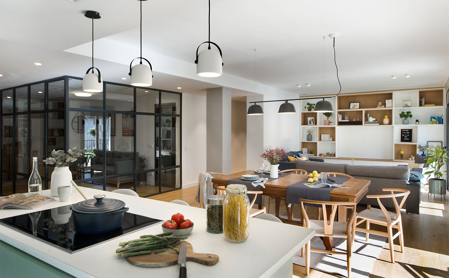 Encimera de isla de cocina en blanco, con luminarias suspendidas en blanco, comedor y salón al fondo 