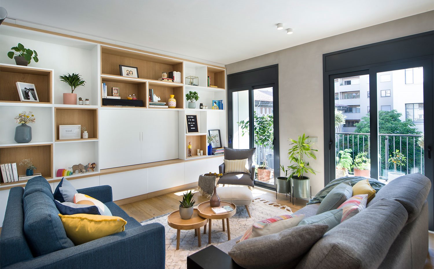 Salón con librería a medida en madera, sofás en azul y gris, mesas de centro en madera, butaca gris con reposapiés en crudo