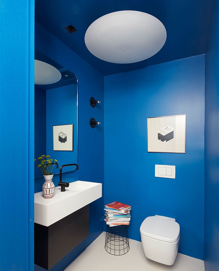 Aseo con paredes y techos de color azul, encimera y sanitario en blaco y módulo bajolavabo en negro