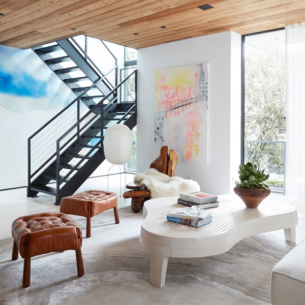 Salón con sofá blanco, taburetes de piel marrón, mesa de centro blanca, alfombra gris y techo recubierto de madera 