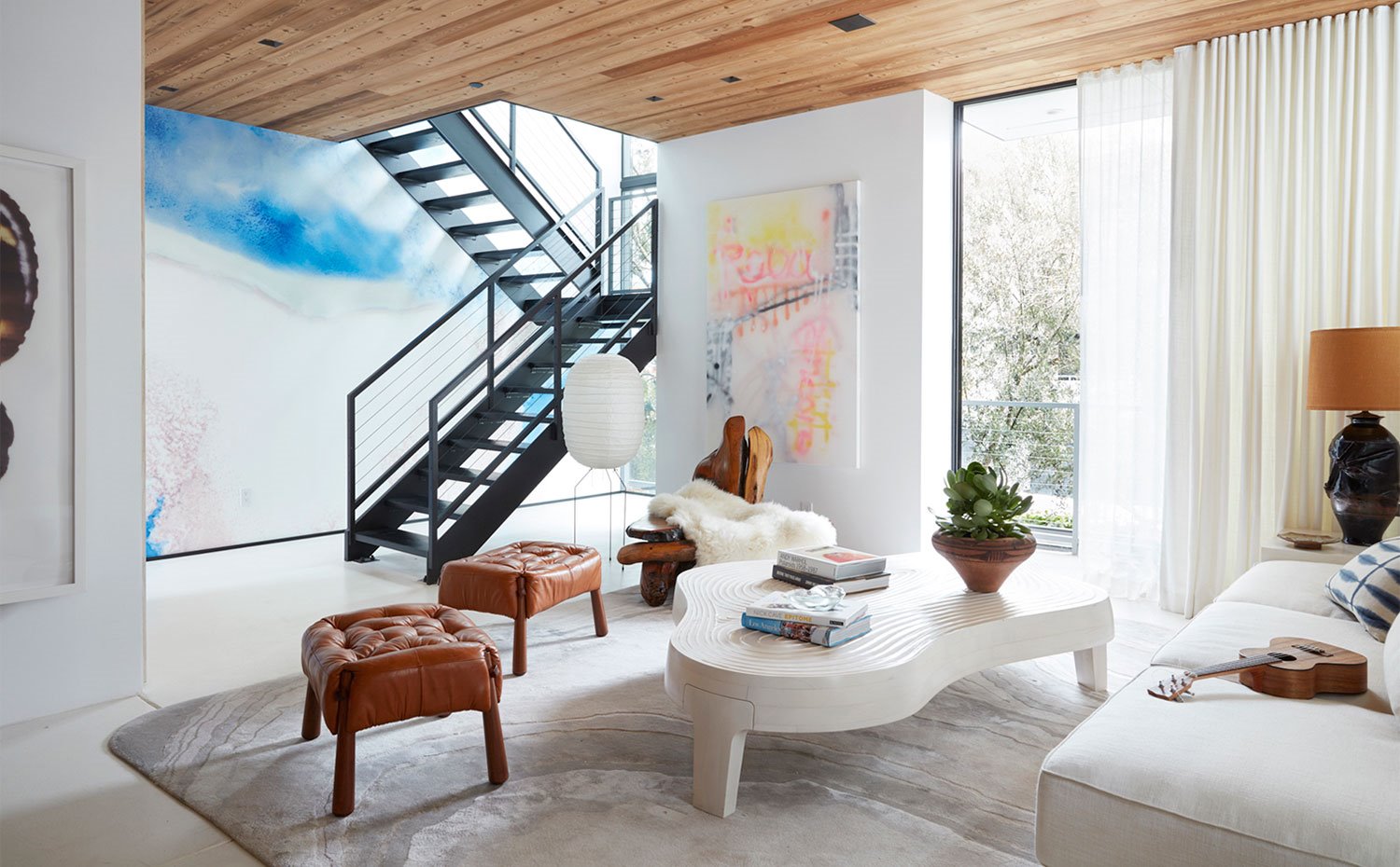 Salón con sofá blanco, taburetes de piel marrón, mesa de centro blanca, alfombra gris y techo recubierto de madera 