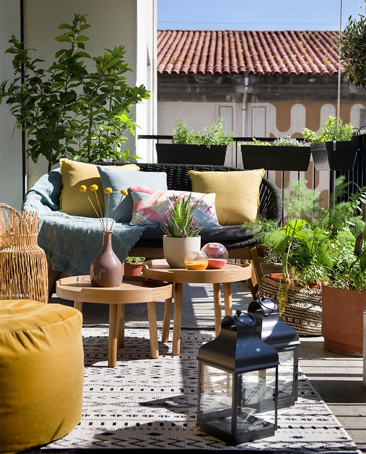 Terraza con butaca de fibras naturales, pouf en tonos mostaza, mesas en madera, candelabros cromados
