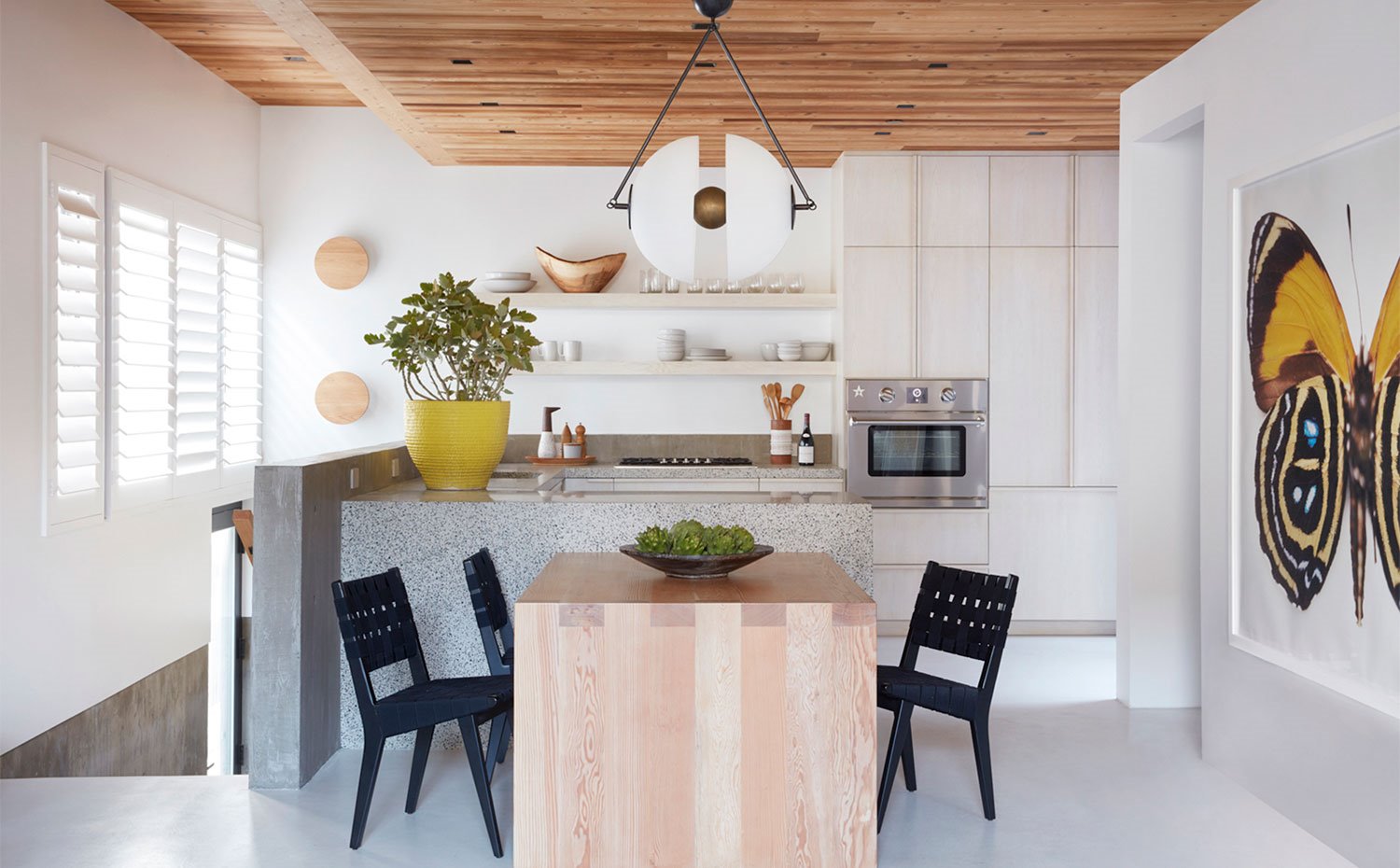 Zona de cocina abierta con península en granito y mesa de comedor en madera con sillas en negro