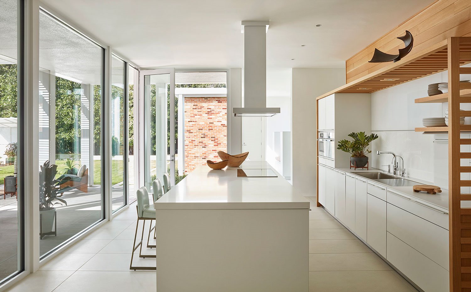 Cocina con isla central, todo en blanco, con estructura superior en madera, cerramientos acristalados