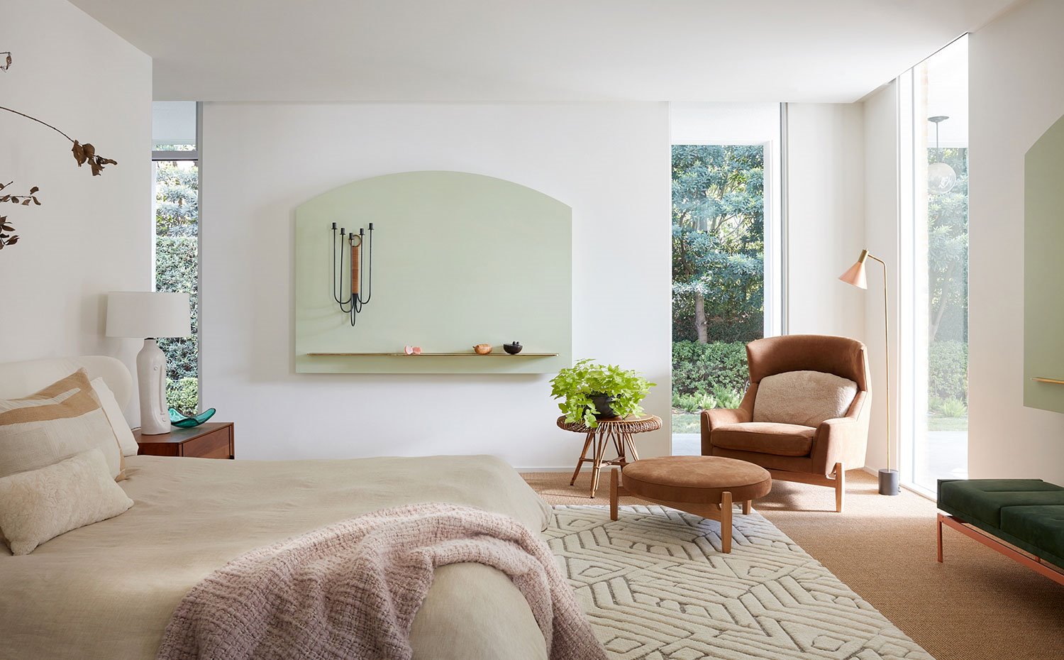 Dormitorio con cama en tonos crudos, alfombra con motivos geométricos, butaca y pouf en marrón, bancada en gris y madera