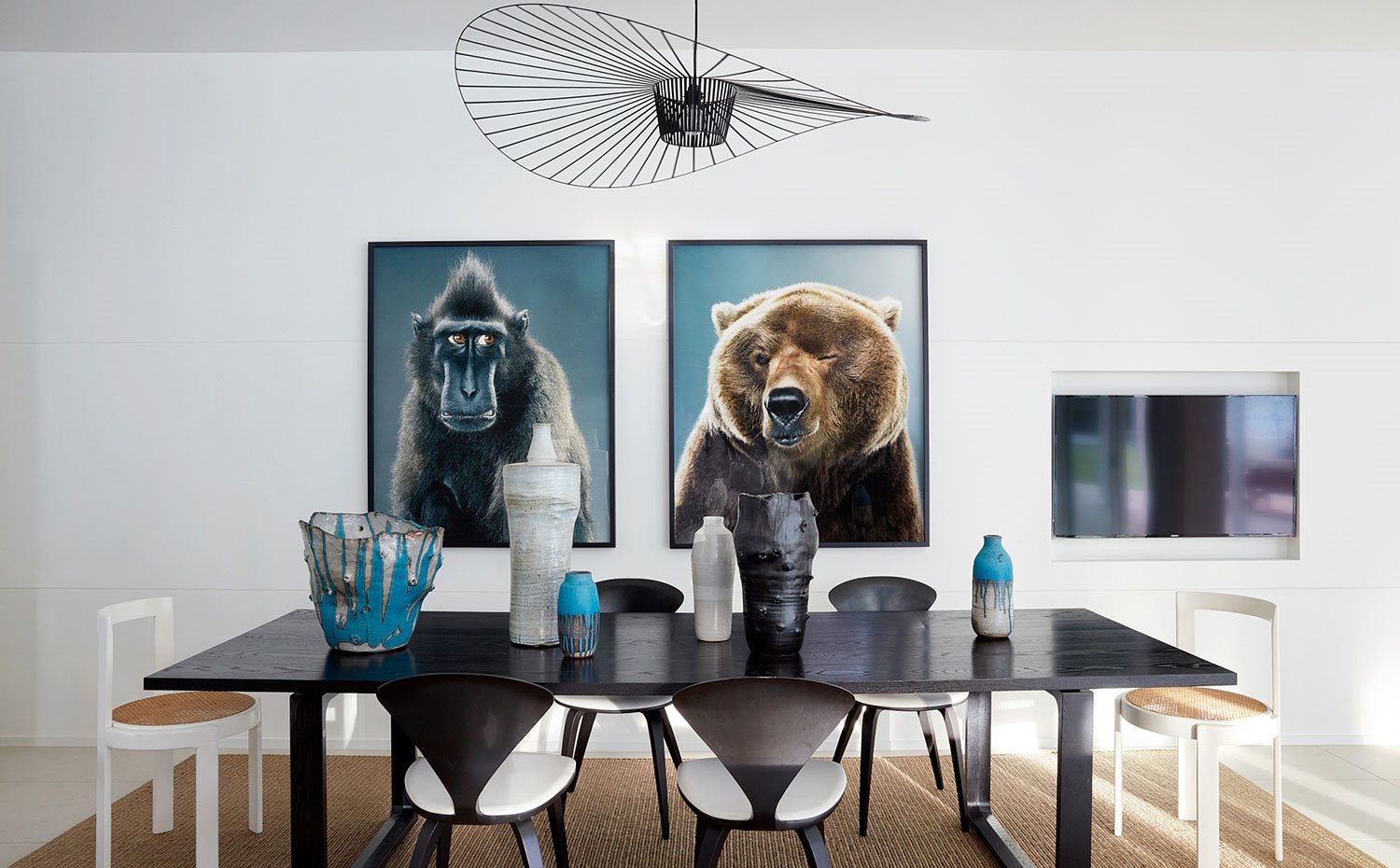 Mesa de comedor rectangular en negro con sillas en blanco y negro, piezas escultóricas en iazul, gris, negro y blanco