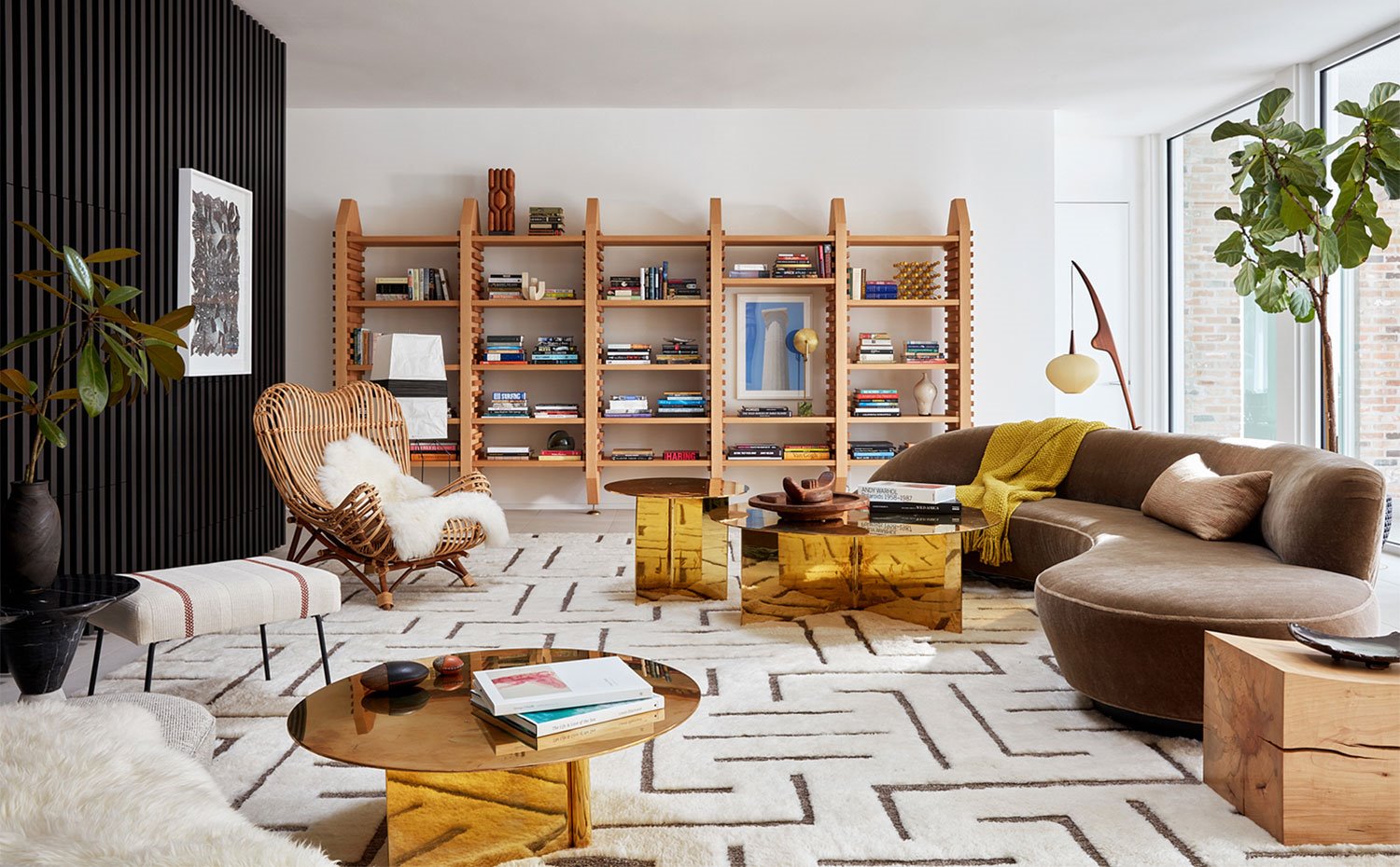 Salón con sofá curvo en marrón, butaca en fibras naturales, mesas doradas, librería de madera