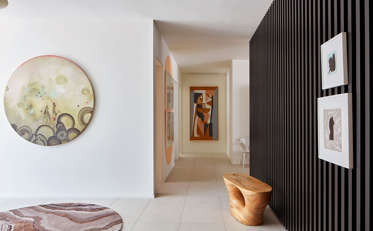 Zona de paso con tabique alistonado en negro, asiento en madera, esculturas y obras gráficas en pared