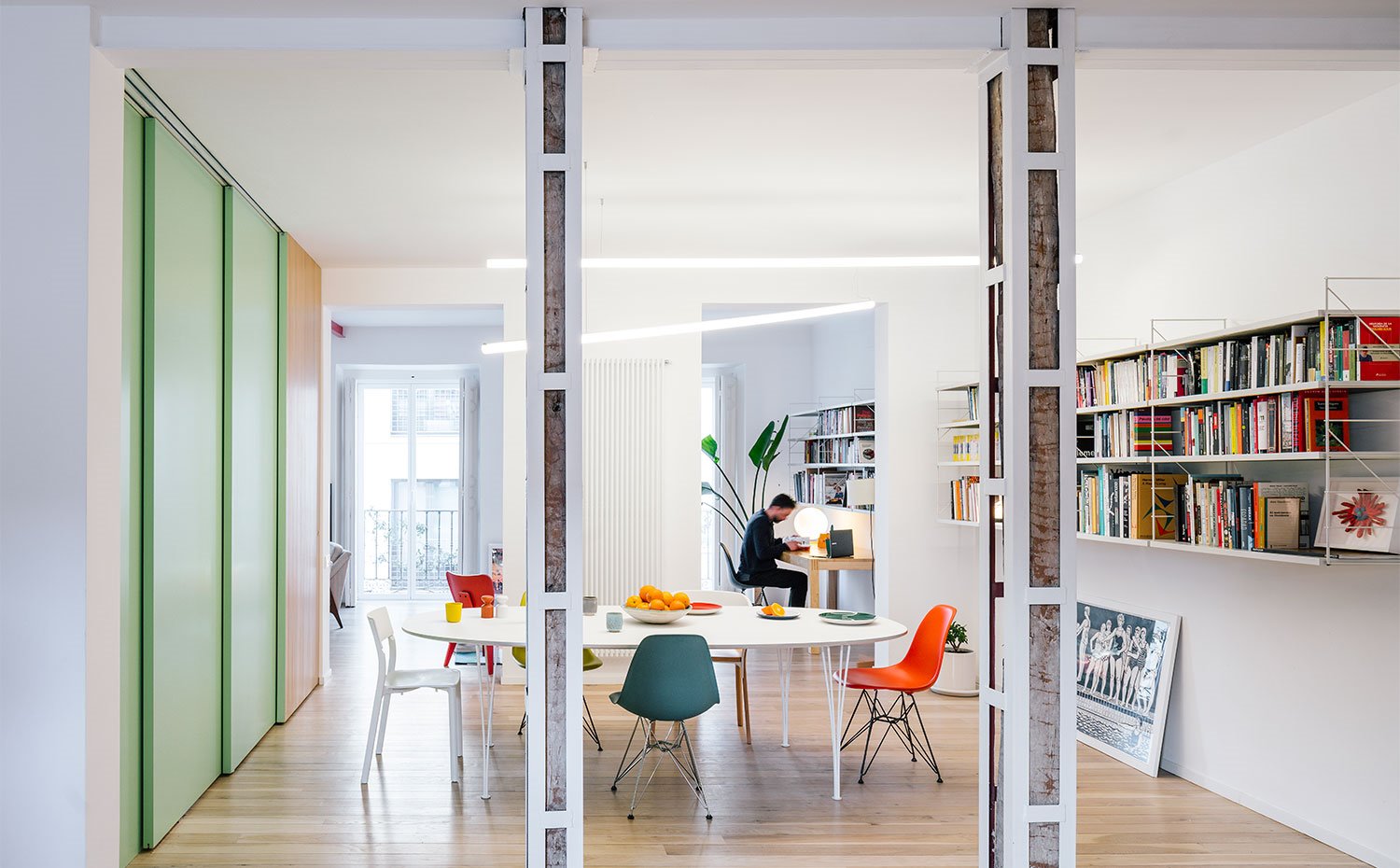Mesa comedor, estantería de pared suspendida, columnas revestidas de estructura en blanco, puertas correderas en verde claro