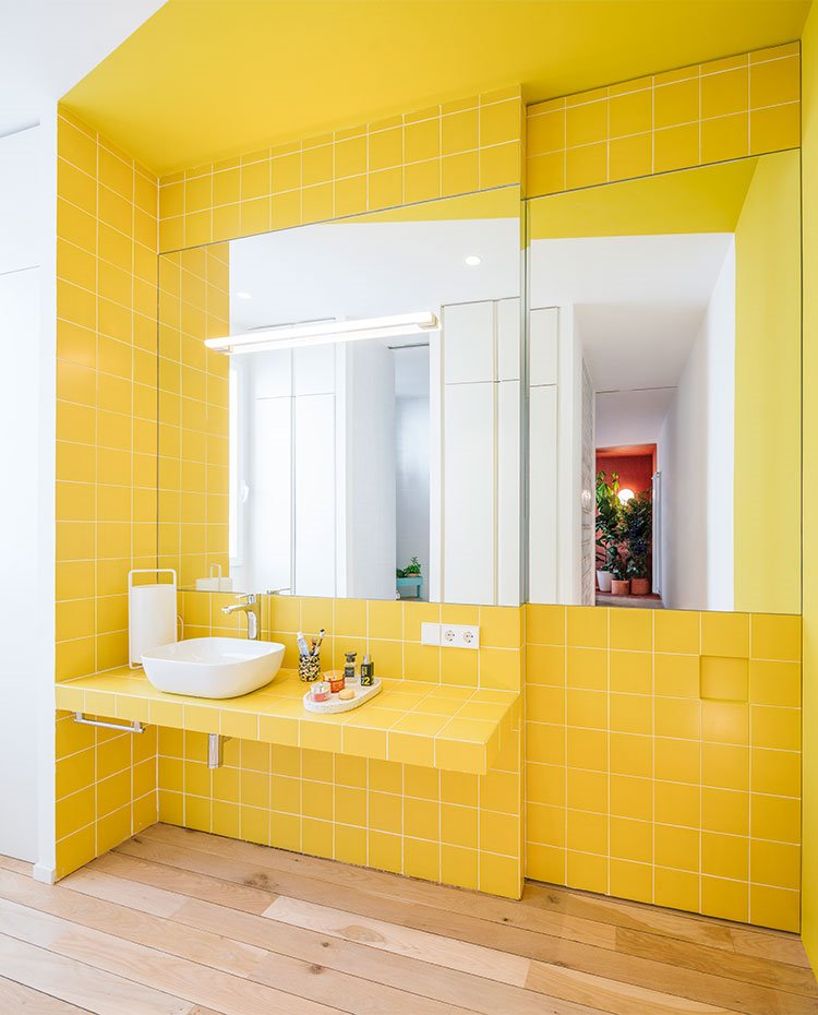 Zona de lavamanos de cuarto de baño con pared revestida de baldosas amarillas, encimera de obra