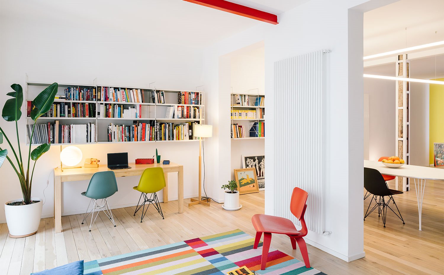 Zona estudio con sillas en verde y turquesa, butaca de madera roja y viga roja en techo