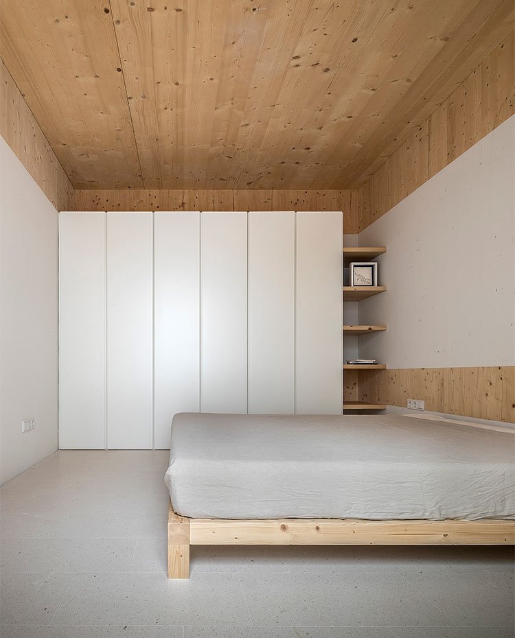 Dormitorio con cama de madera y armarios en blanco con estanterías en extremo