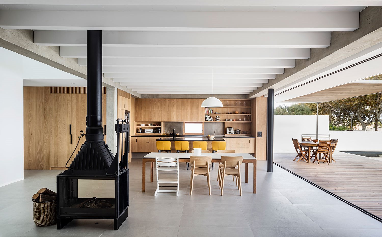 Chimenea de hierro junto a comedor y cocina, con techo de vigas en blanco