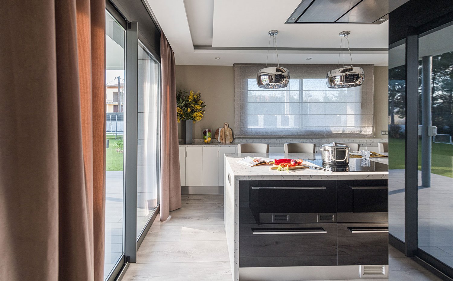 Cocina con isla central con mobiliario en negro y encimera en ocre, luminarias suspendidas cromadas