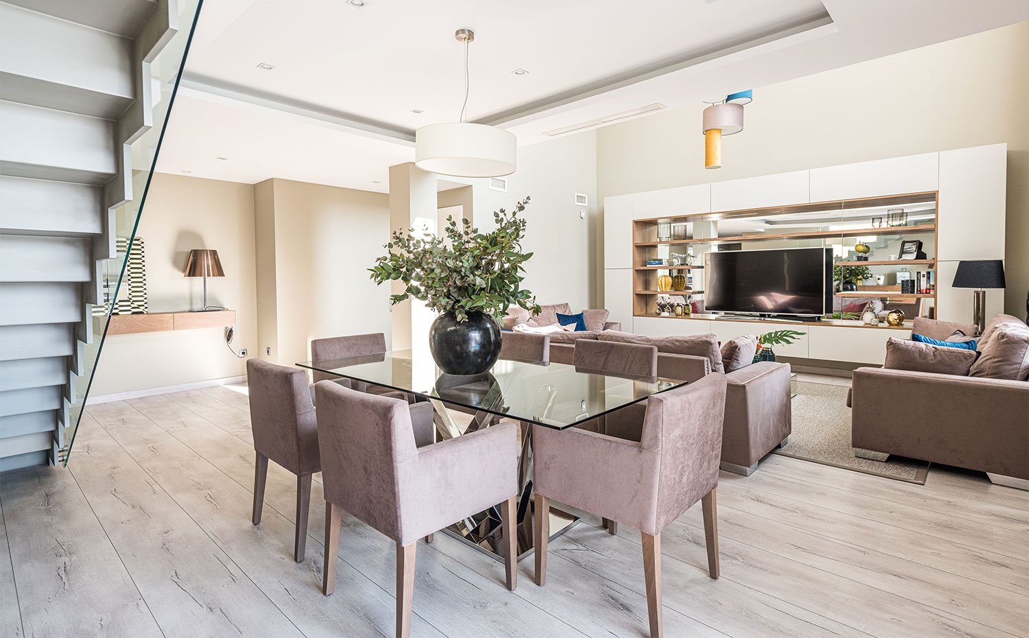 Comedor con mesa rectangular con sobre de cristal, sillas en marrón, suelo de madera, hueco bajo escaleras