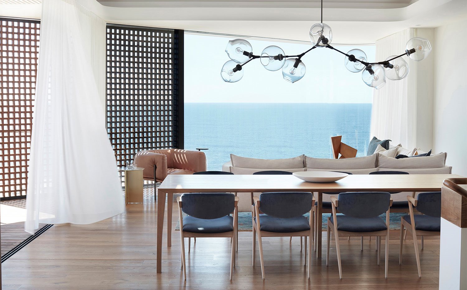 Comedor y salón con cerramientos de cristal, estructuras a modo de celosía y cortinas en blanco