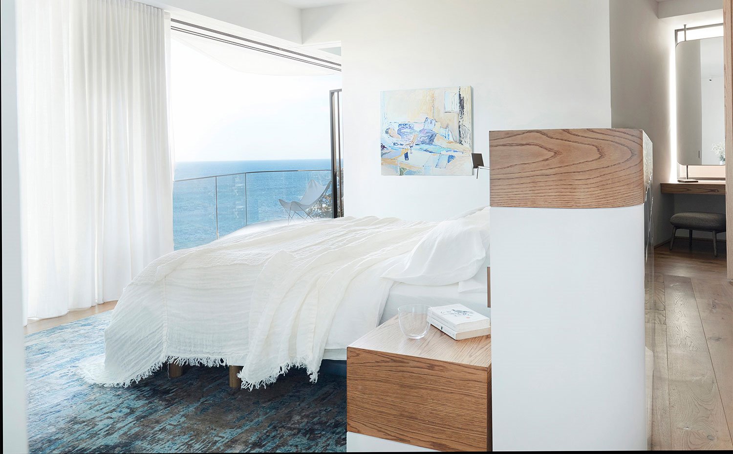 Dormitorio con alfombra en azúl, estructura cabecero con cantos curvos en acabado blanco y madera