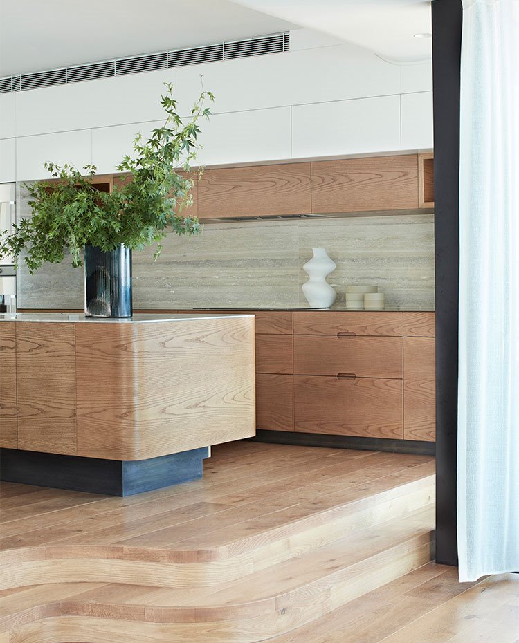 Escaleras recubiertas de madera hacia cocina abierta con cantos curvos