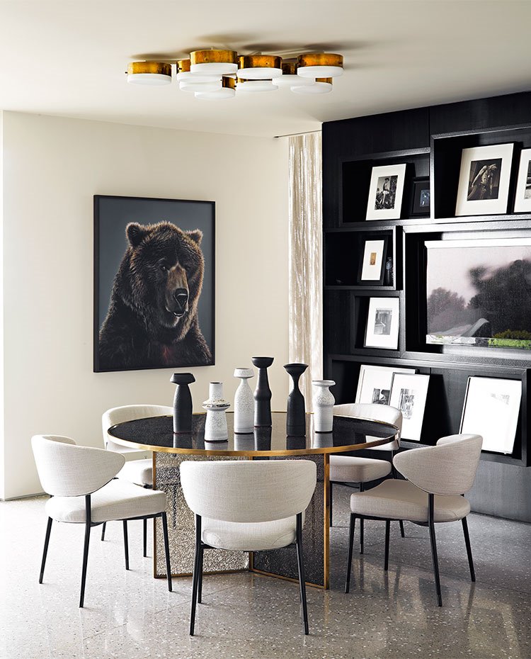 Comedor informal en cocina con mesa circular, sillas en crudo, jarrones sobre mesa en blanco y negro, estantería en negro con televisor integrado