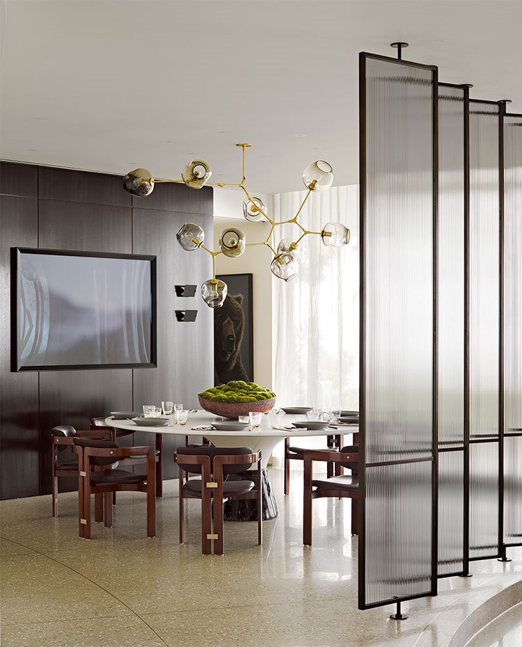 Comedor tras paneles de cristal esmerilado, mesa circular y sillas en madera y tapizadas en piel negra