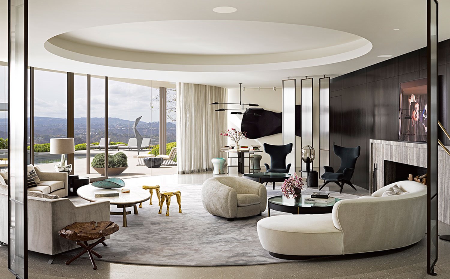 Salón con disposición circular, cerramientos de cristal, mobiliario contemporáneo con sofás curvos y chimenea revestida de mármol