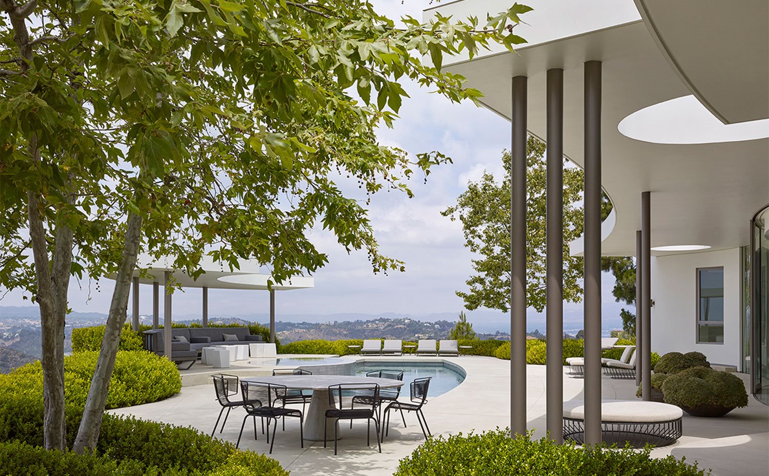 Terraza exterior con mesa de comedor y zona con porche con poufs y tumbonas tapizadas en color crudo