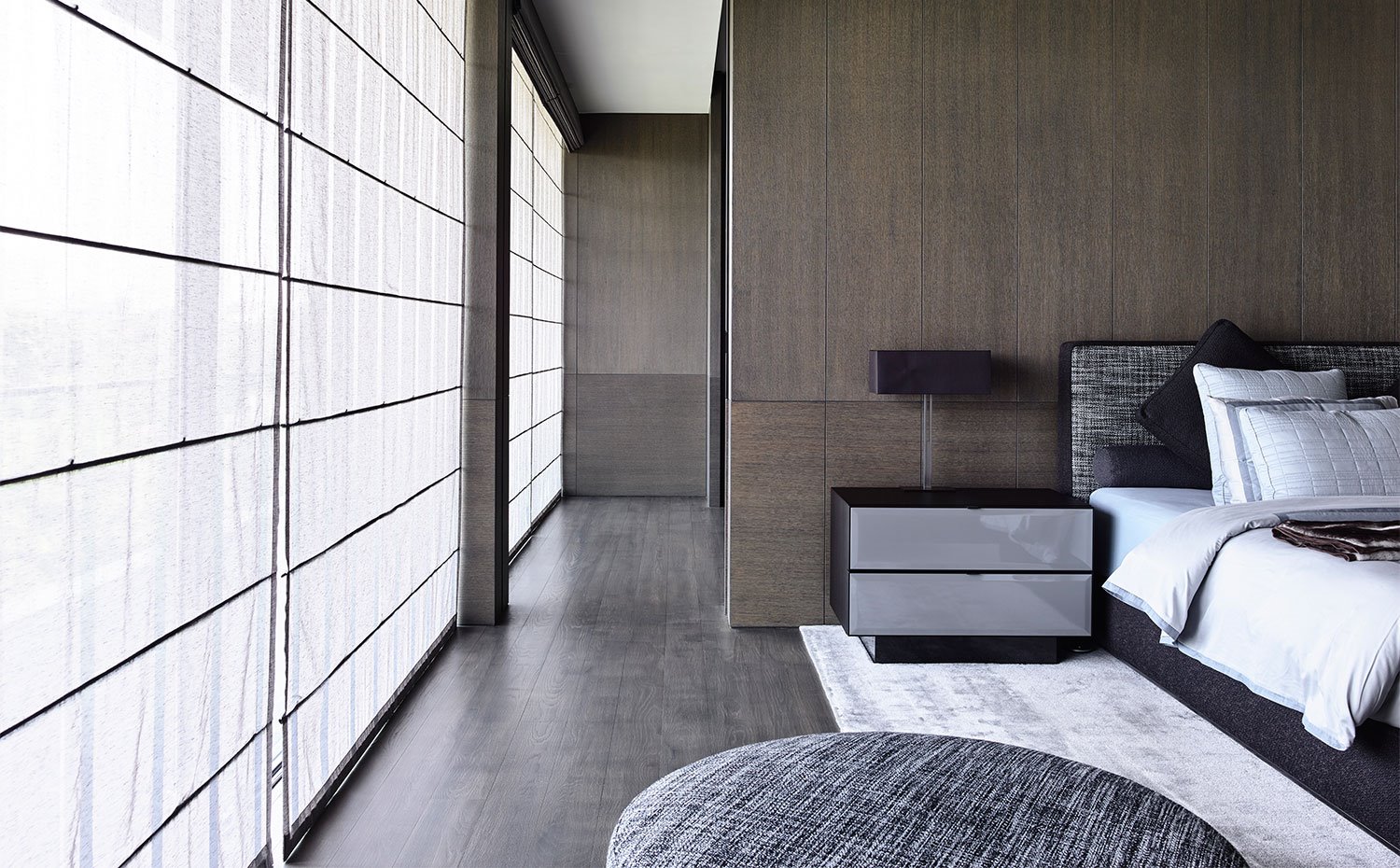 Dormitorio con paredes revestidas de madera, estores plegables de tela frente a cerramientos de cristal