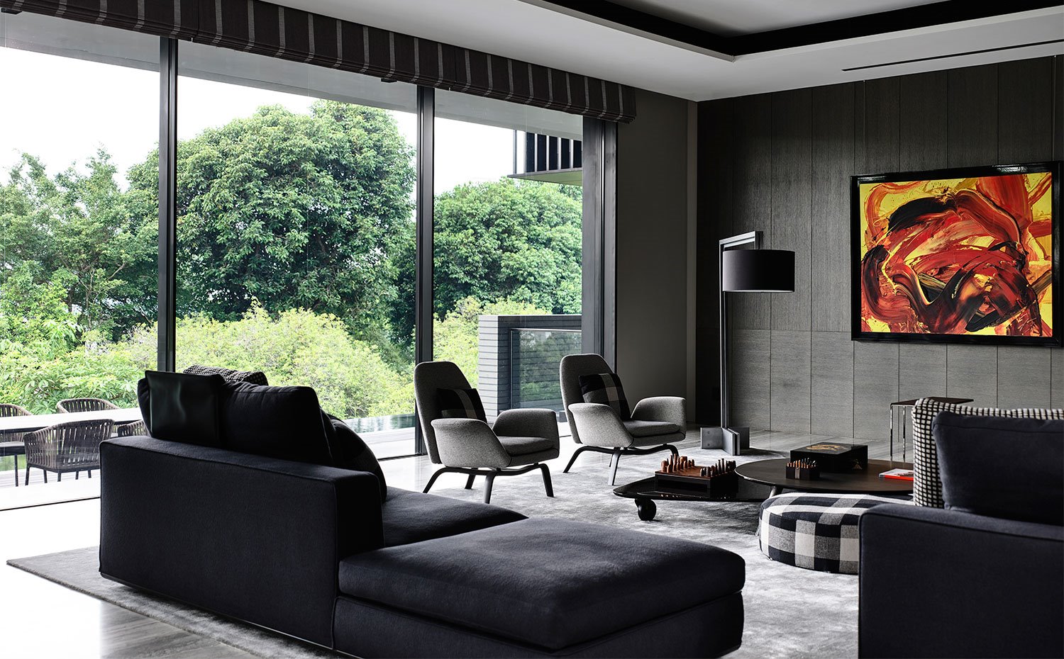 Salón con sofás en negro, butacas en gris, y mesas de centro con cantos curvos, cuadros en pared de colores vivos