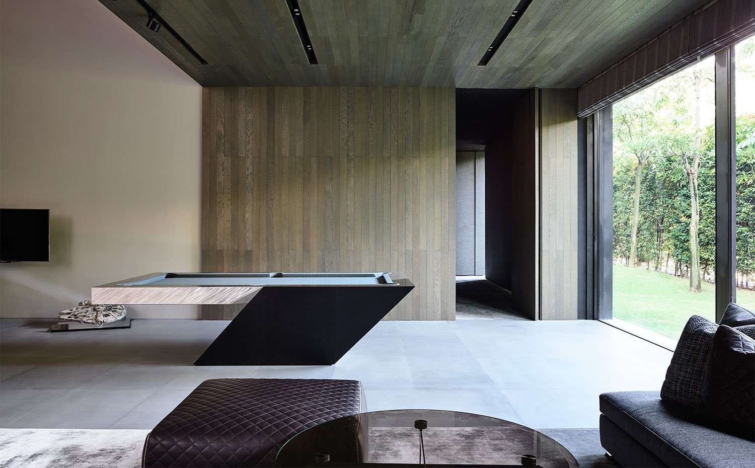 Zona de ocio con billar y sofás y poufs en tonos oscuros, revestimientos de madera