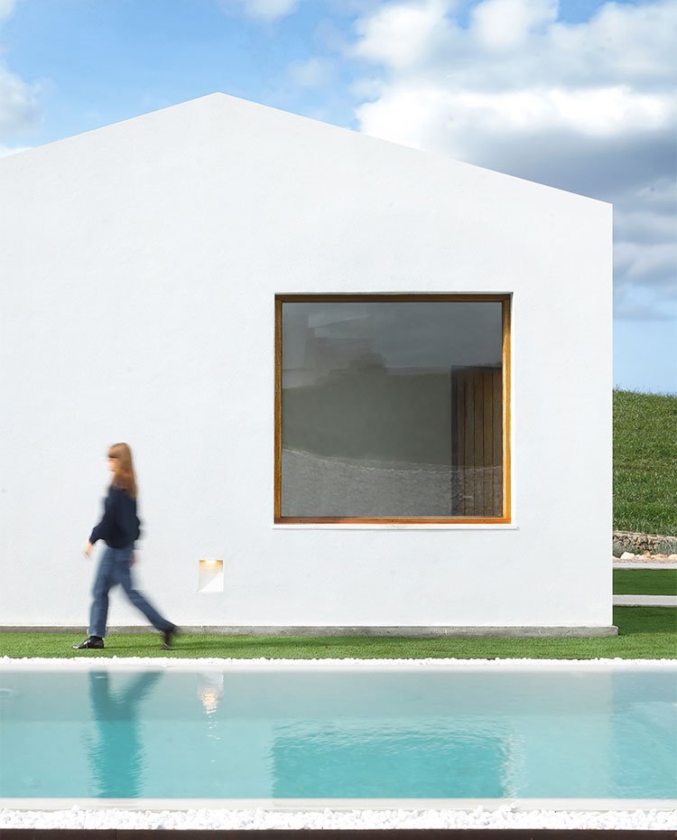 Exterior de caseta con ventana cuadrada y piscina con piedra de canto rodado alrededor