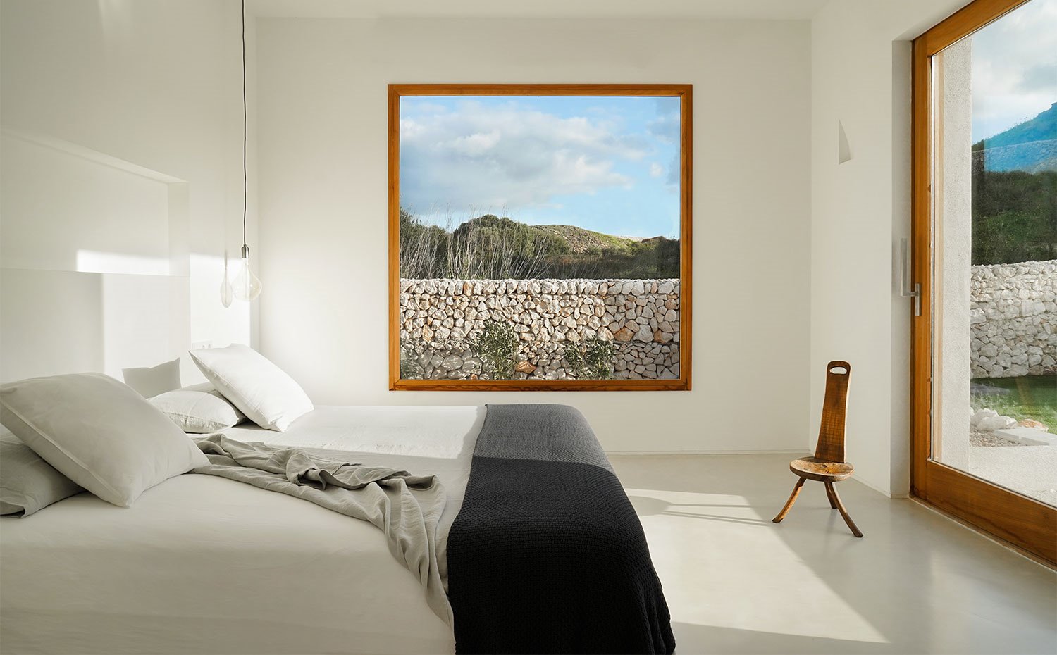 Interior dormitorio en blanco, con grandes cerramientos y vistas al exterior 