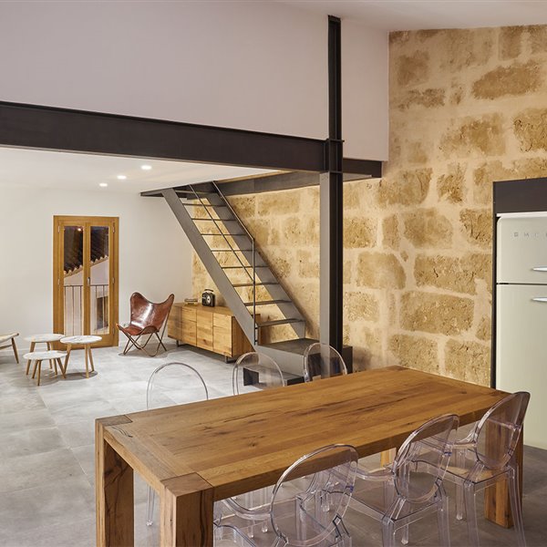 Cocina abierta con mobiliario en negro y frigorífico en ocre, mesa de madera y sillas transparentes
