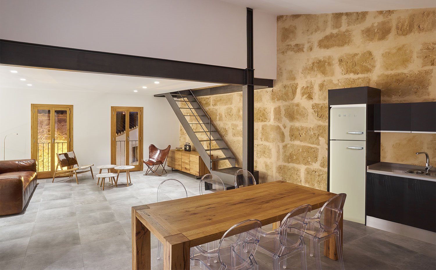 Cocina abierta con mobiliario en negro y frigorífico en ocre, mesa de madera y sillas transparentes