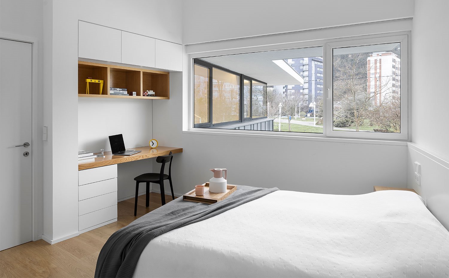 Dormitorio con amplia apertura horizontal hacia el exterior, mobiliario integrado en blanco con acabados en madera natural