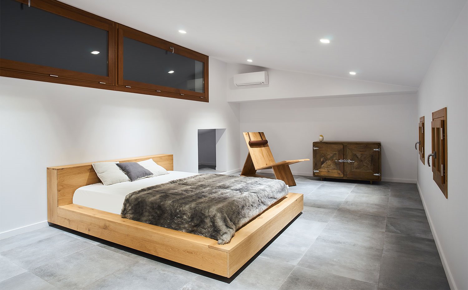 Dormitorio principal con estructura de cama de madera natural y suelo cerámico en gris