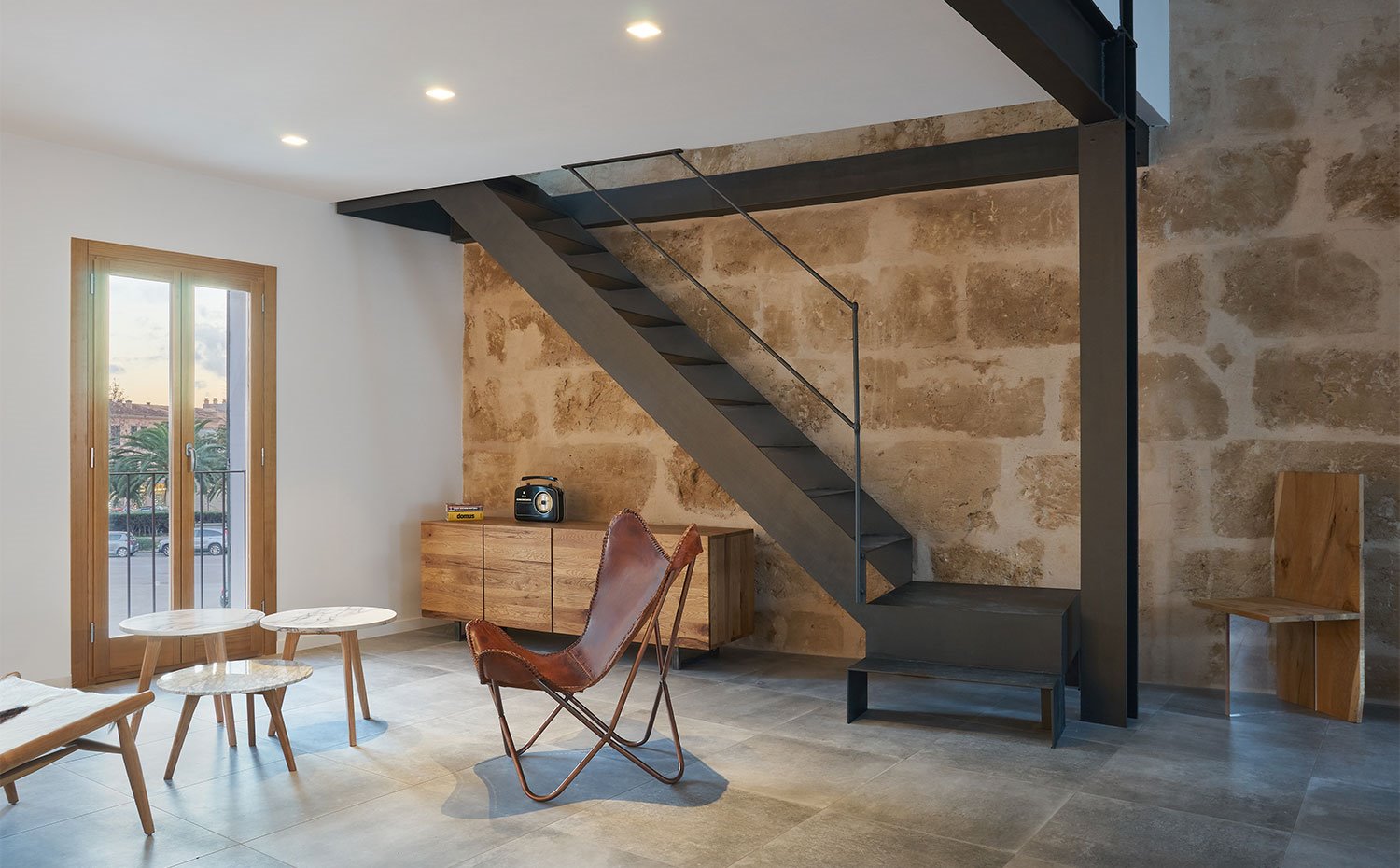 Escaleras y vigas de acero negro con pared de piedra vista, perfilería de madera