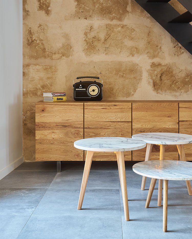 Mesitas auxiliares de sobre de mármol con patas de madera, mueble de madera frente a pared revestida de piedra