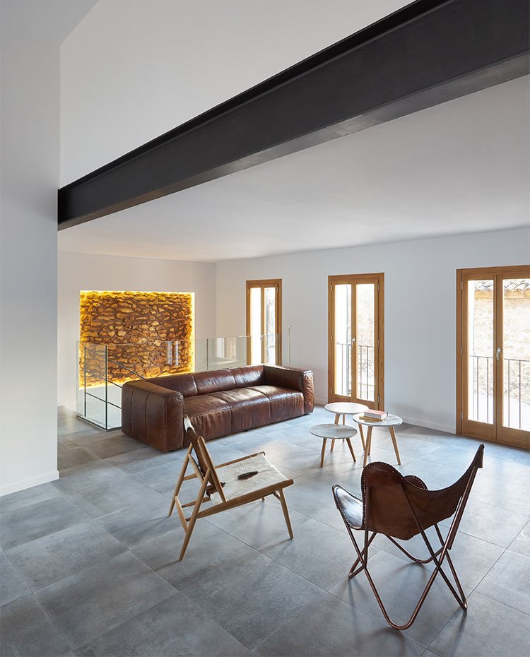 Salón con sofá de piel marrón, butaca marrón y de piel de baca, perfilería de madera, viga de hierro