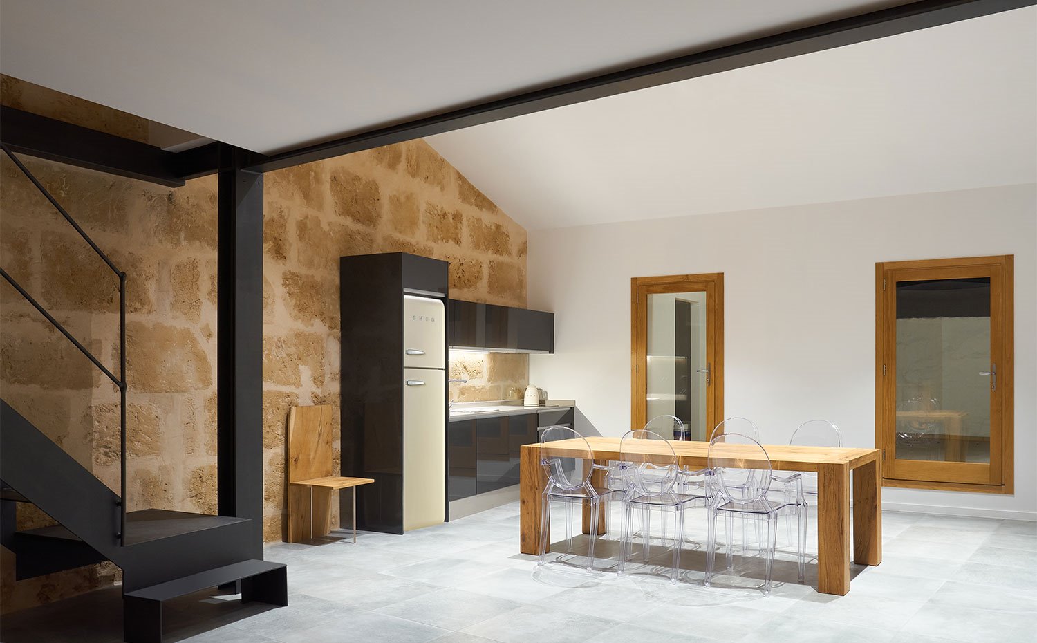 Vigas de hierro negro, pared de piedra vista, mesa de comedor de madera y sillas de plástico
