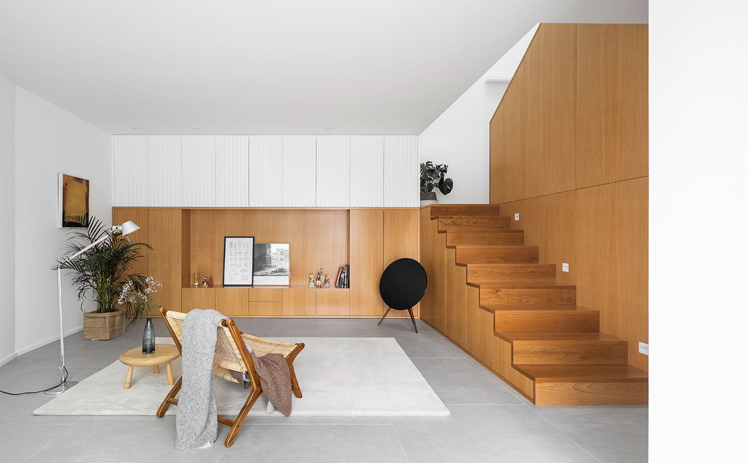 Zona de estar con butaca en madera y fibras naturales, alfombra en blanco, luminaria de suelo y mobiliario en madera, hecho a medida en acabado natural