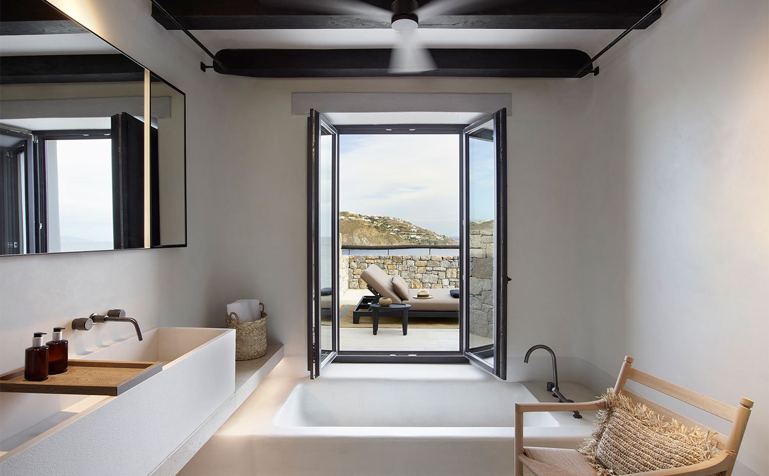 Cuarto de baño con amplia zona de lavamanos, y bañera de formas cuadradas con amplia ventana abierta con vistas al exterior