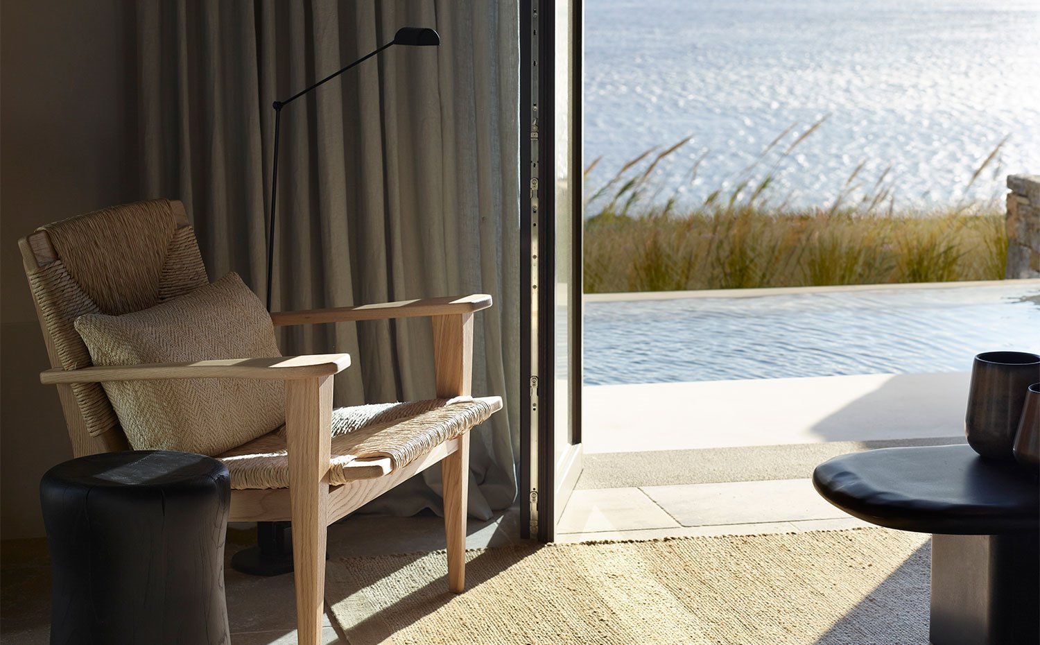 Detalle asiento de madera y fibra natural junto a cerramiento acristalado junto a piscina exterior